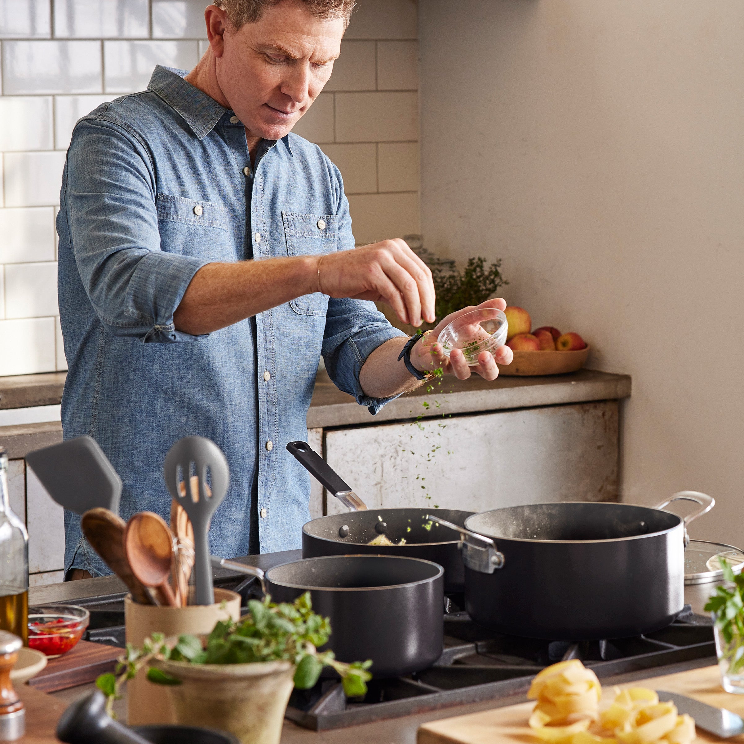 Man cooking with GreenPan 16-piece cookware set; utensils, spices, and pots visible on the kitchen counter.