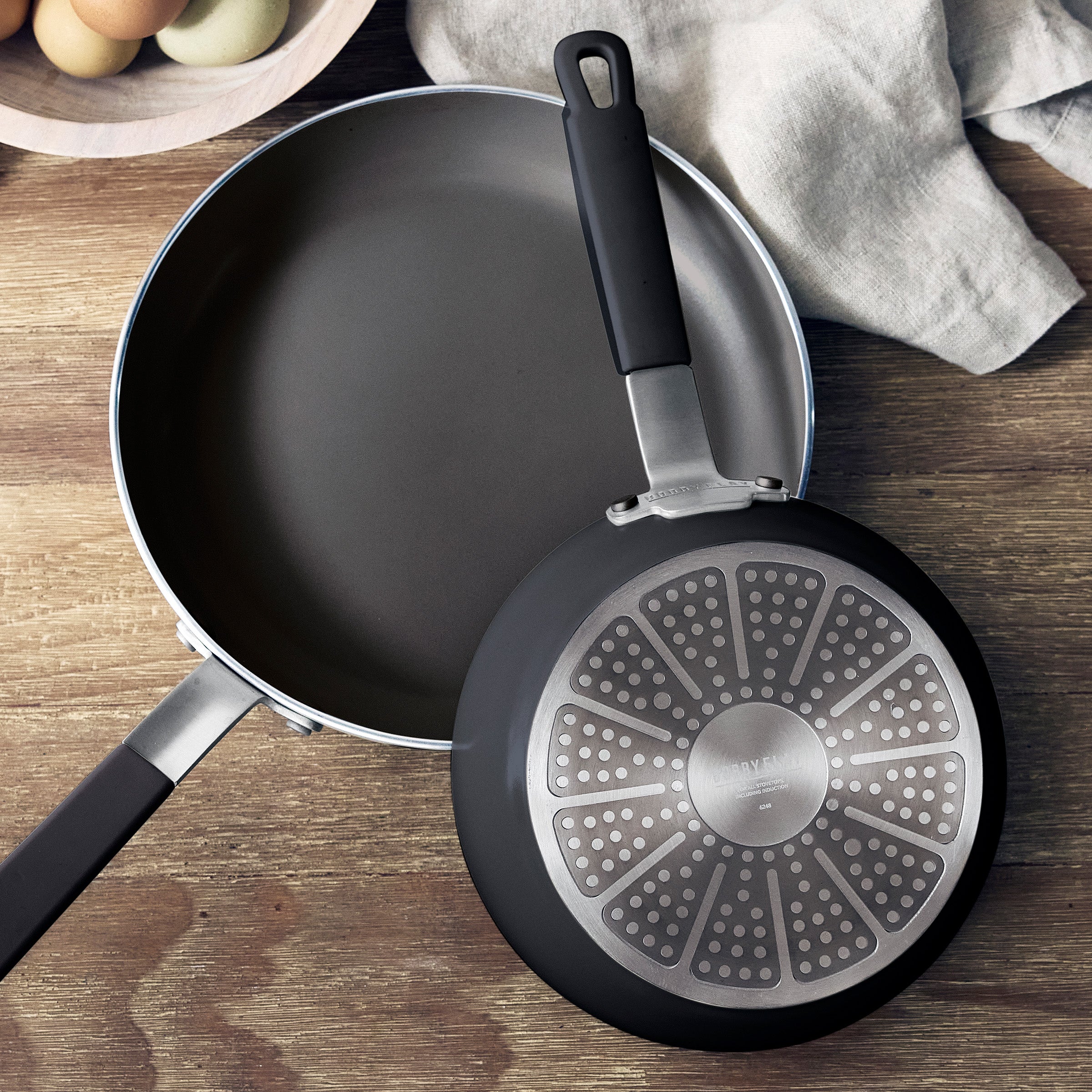 Two GreenPan nonstick pans on a wooden surface, one upright showing the interior, one flipped to show the base. Set of 2.