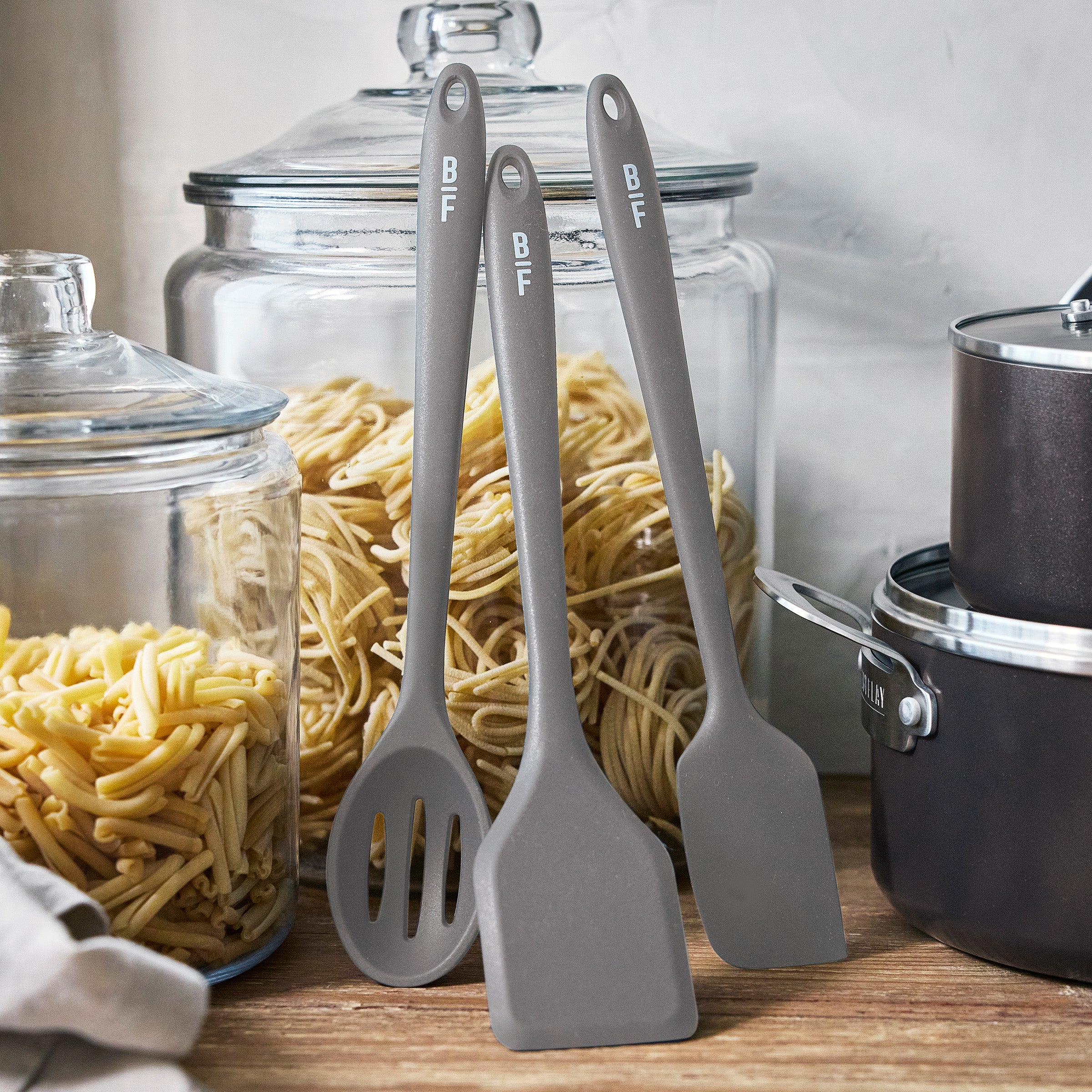Graphite kitchen utensils next to a 16-piece Bobby Flay by GreenPan cookware set and jars of pasta.