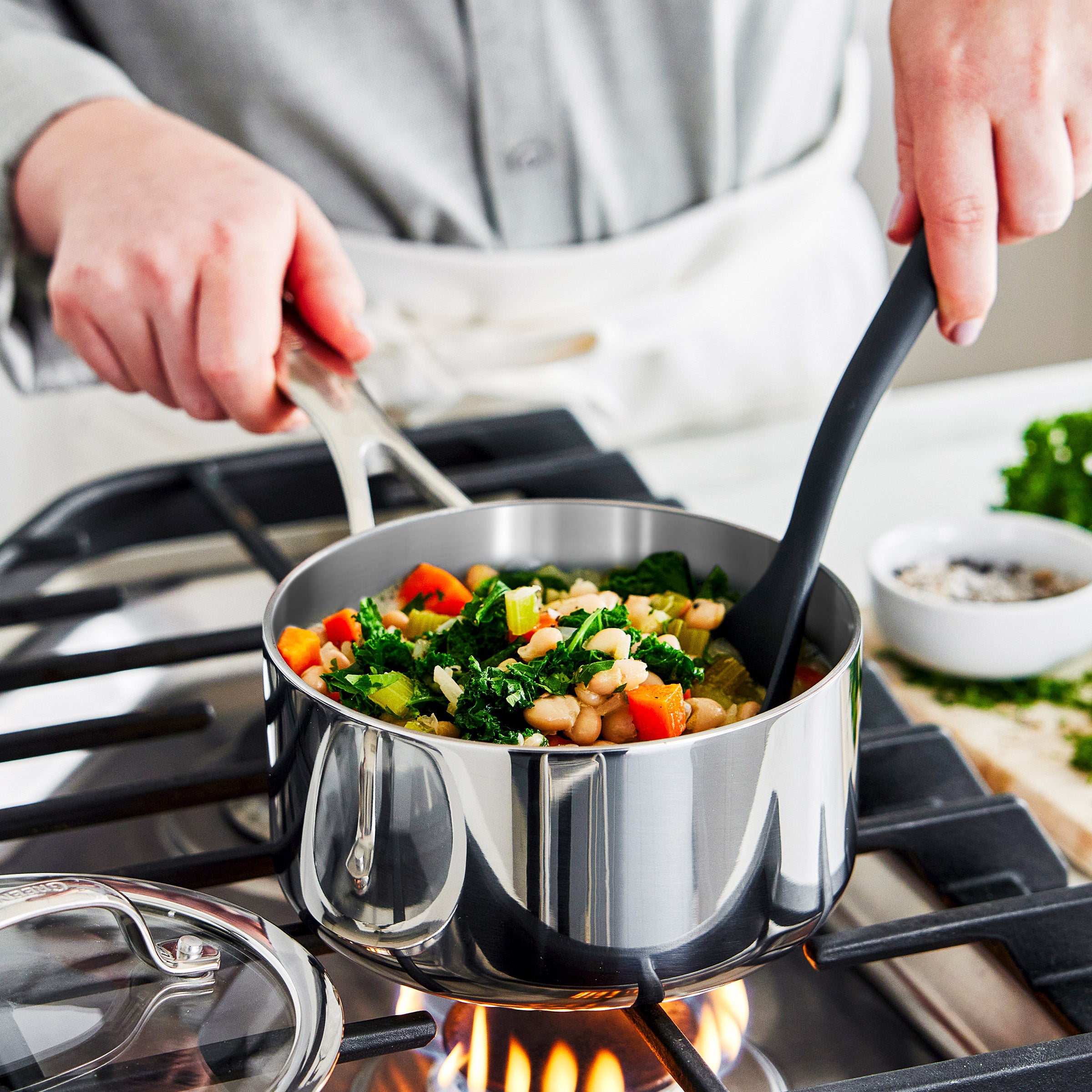Stirring a pot of food on a stove with a person wearing an apron.