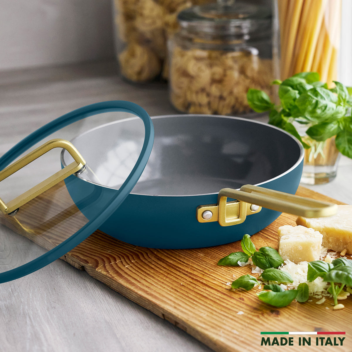 Stanley Tucci 3.25-quart ceramic nonstick Piccolo pan in Venetian teal with a glass lid and gold-tone handles on a wooden cutting board.