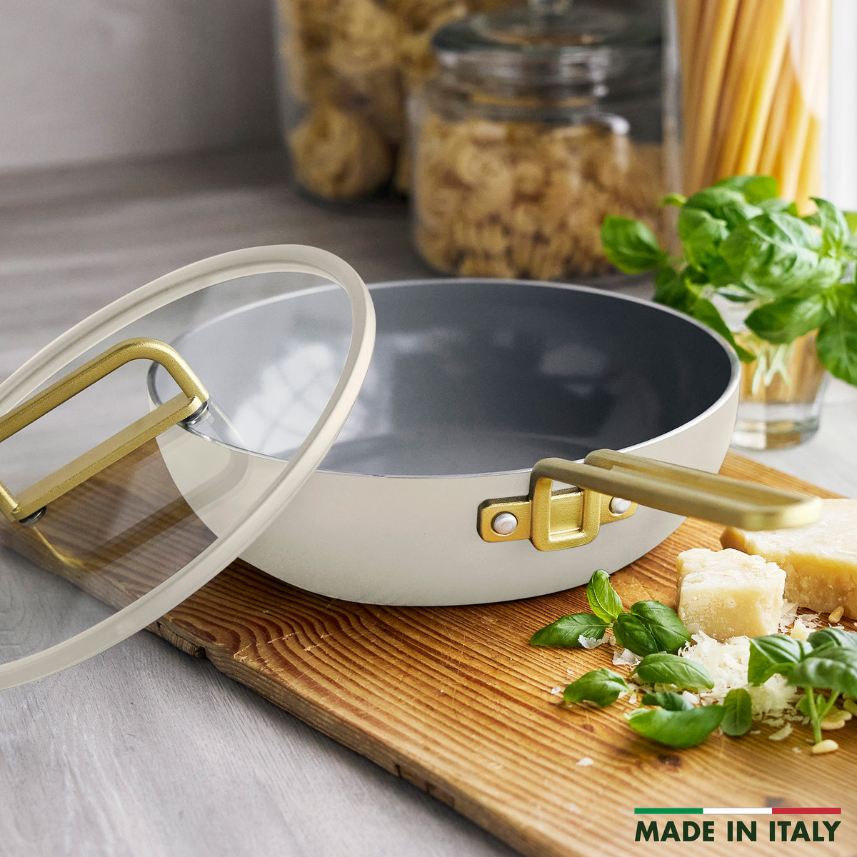 Stanley Tucci 3.25-quart ceramic nonstick Piccolo pan in Carrara white with a glass lid and gold-toned handles on a wooden board.