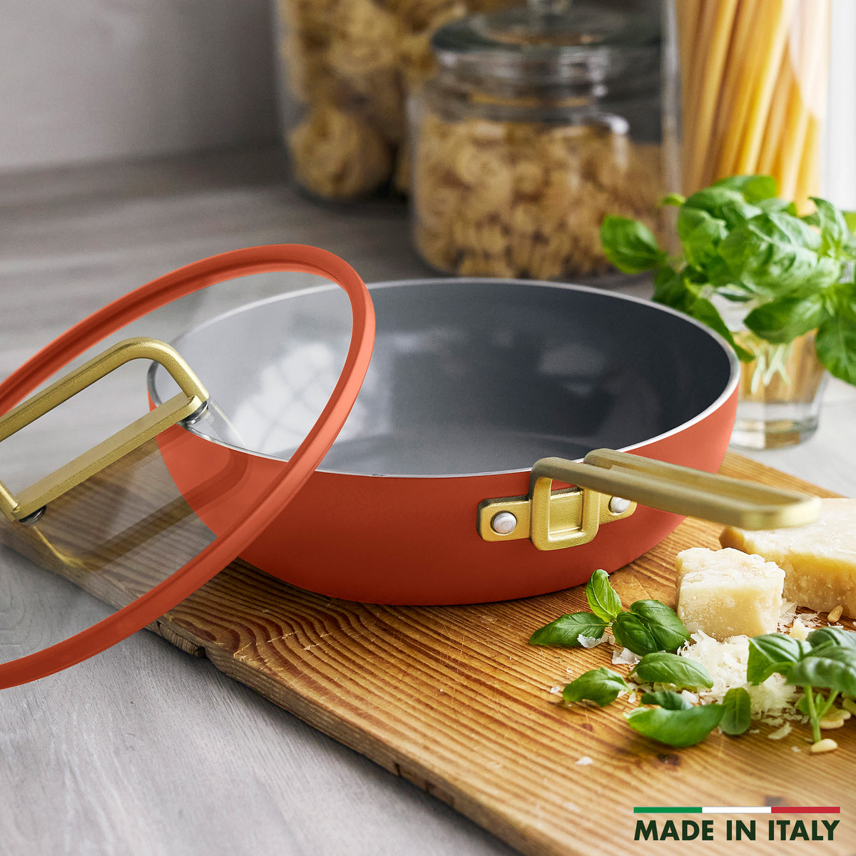 Stanley Tucci 3.25-quart ceramic nonstick piccolo pan in Amalfi Sunset with glass lid and gold-tone handles on a wooden board.