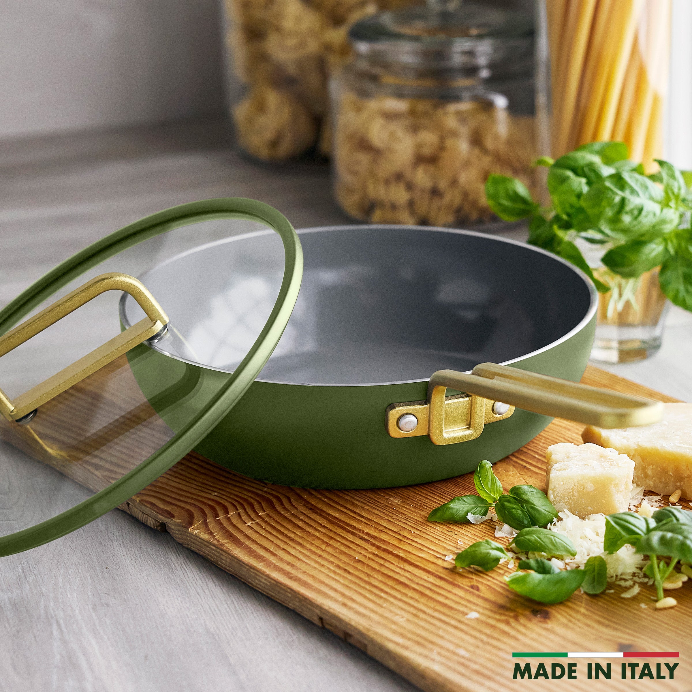 Green Tuscan olive saucepan with gold handles on a wooden board, garnished with basil and cheese.
