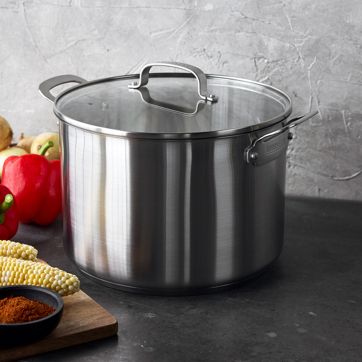Bobby Flay by GreenPan 12-quart uncoated stainless steel stockpot with glass lid next to fresh vegetables.