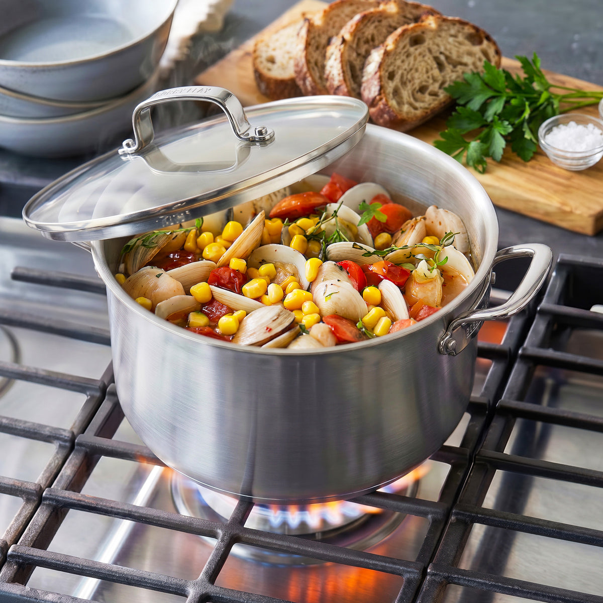 Bobby Flay by GreenPan 12-quart stainless steel stockpot with lid, filled with clam, corn, and tomato stew on a gas burner.