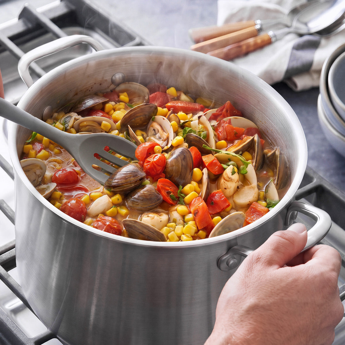 Grey silicone slotted spoon stirring stew in a Bobby Flay by GreenPan uncoated stainless steel 12-quart stockpot with lid.