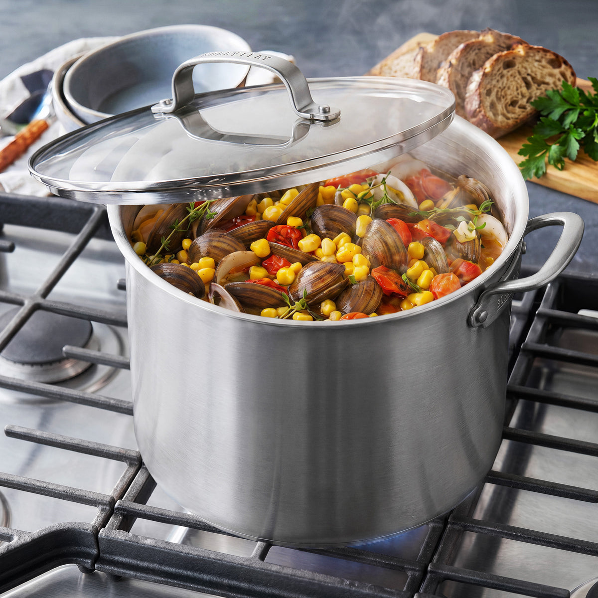 Bobby Flay by GreenPan 12-quart stainless steel stockpot with lid, filled with clam, corn, and tomato stew on a gas stovetop.