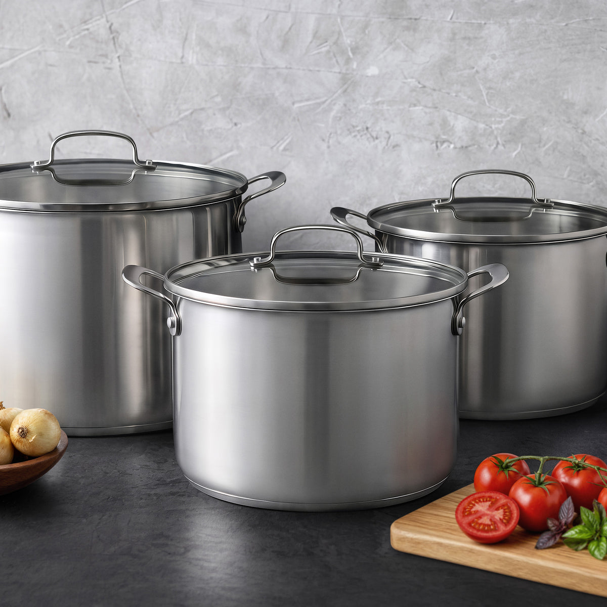 Bobby Flay by GreenPan 16-quart stainless steel stockpot with lid and two matching stainless steel pots on a dark countertop.