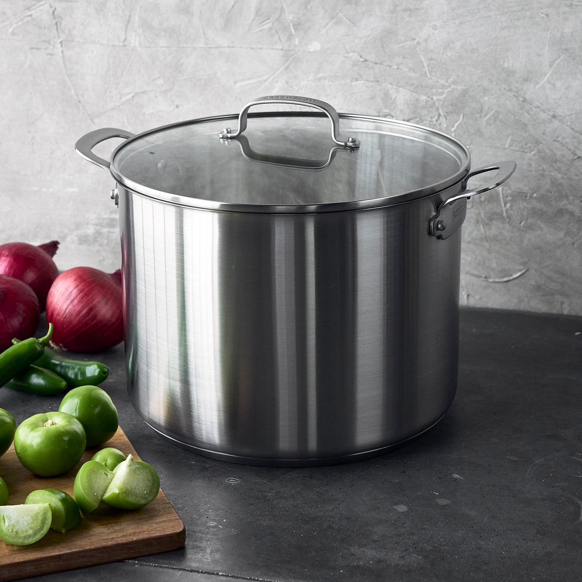 Bobby Flay by GreenPan 16-quart uncoated stainless steel stockpot with lid, sitting on a wooden cutting board with onions and tomatillos.