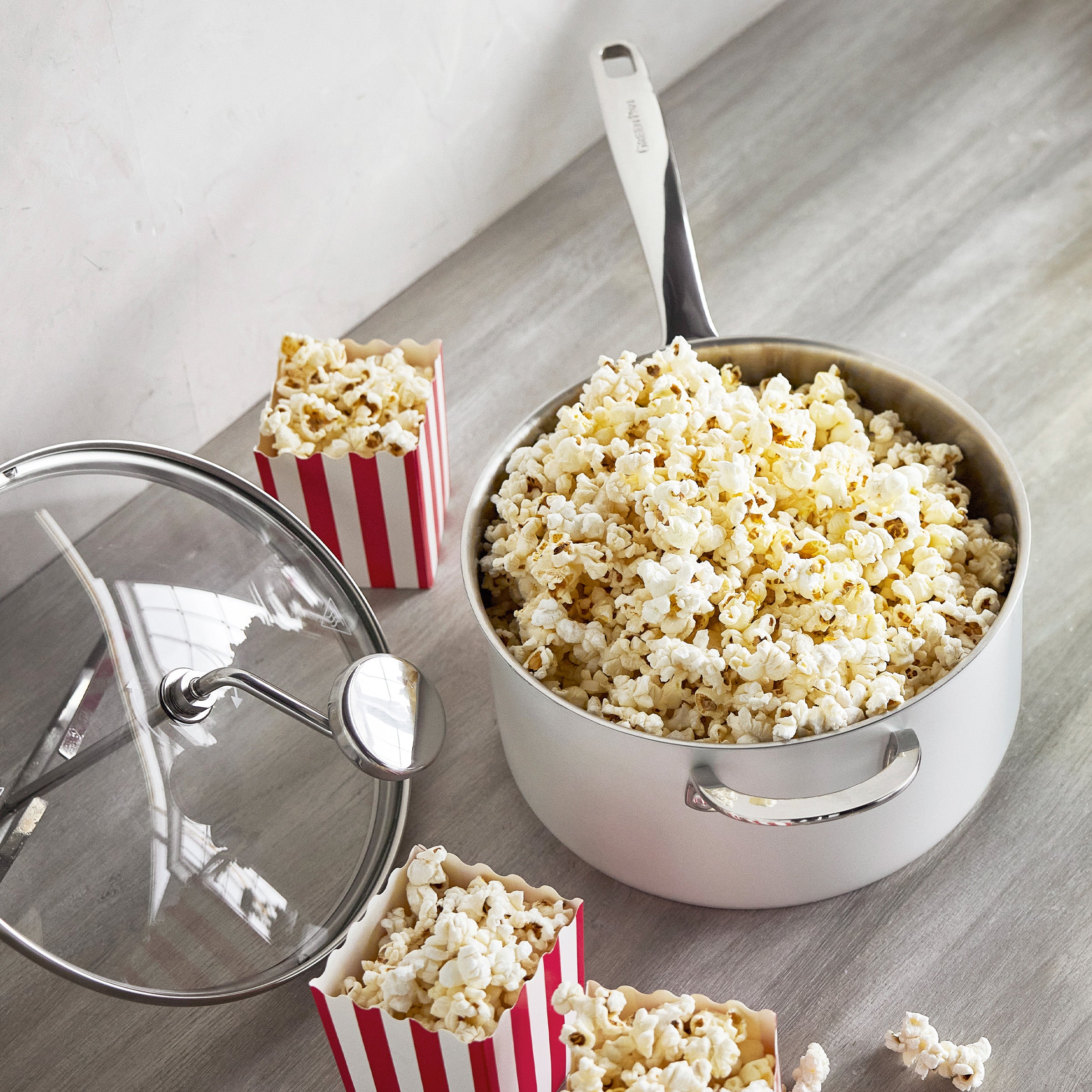 Cream popcorn maker with glass lid on a table, next to red-striped popcorn containers.