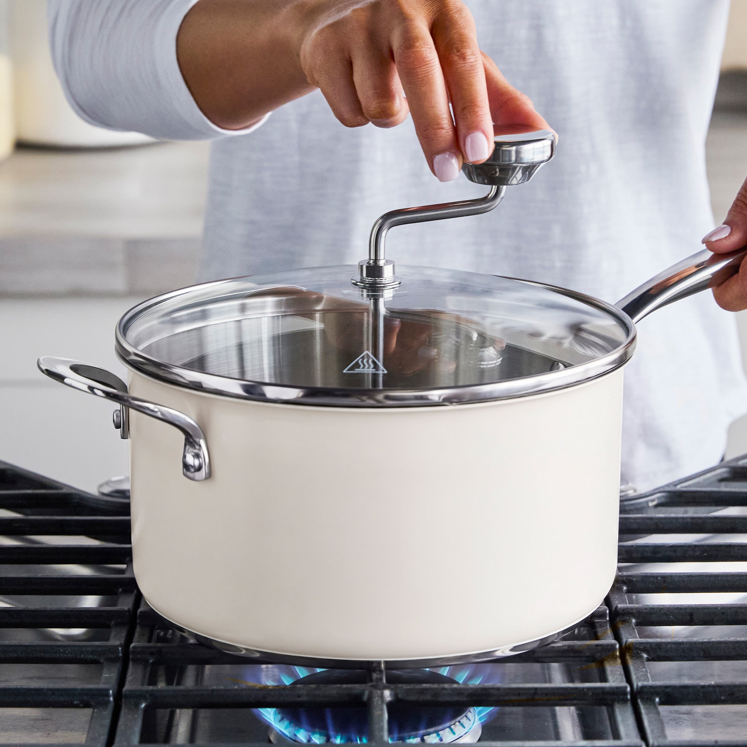 Cream Big Popper Popcorn Maker with glass lid on a gas stove, metal knob being adjusted while popcorn heats inside.