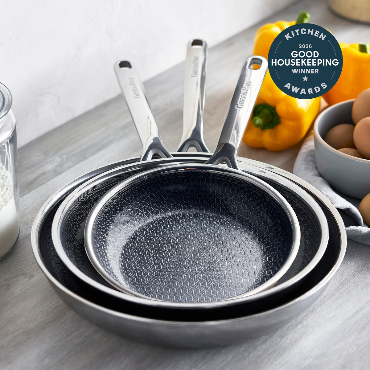 Stacked ceramic nonstick frypan set in three sizes on a counter with eggs, peppers, and an award badge visible.
