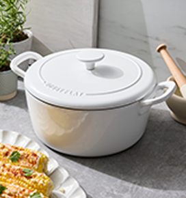 White ceramic pot with a lid on a table with corn on the cob and a plant in the background