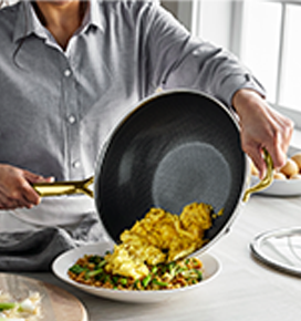 Person serving scrambled eggs from a frying pan onto a plate.